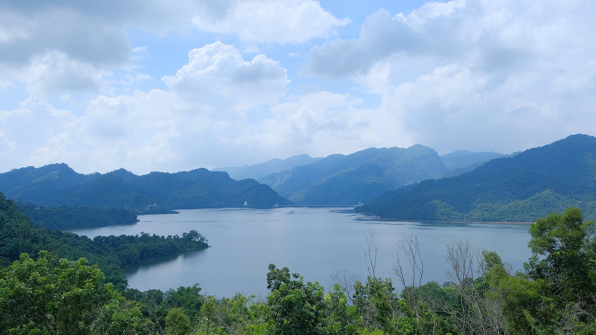 曾文水庫全景,水面在群山之間展開,遠處可以看到壩體與水面上的攔汙索